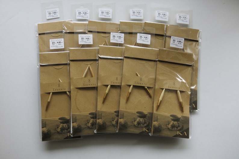 May include: A selection of knitting needles, packaged in clear plastic and brown paper. The needles have light-coloured wooden shafts with gold-coloured tips. Each package has a label with the text "8 Seeknit" and size information.
