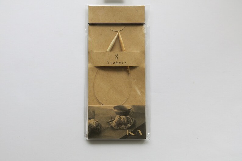 May include: Seeknit circular knitting needles, size 8, in a clear plastic package with a tan paper backing. The needles are made of light-coloured wood and are connected by a flexible cord. The packaging includes a small illustration.