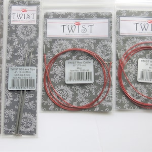 May include: Four packages of interchangeable knitting needles and cables. Two packages contain silver-colored lace tips, one package contains a 30-inch red cable, and one package contains a 37-inch red cable. The packages are labeled "TWIST Red Lace Interchangeables" and include item numbers and sizes.