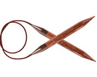 Puede incluir: Un par de agujas de tejer de madera con un cordón rojo que conecta las puntas. Las agujas están cruzadas en forma de 'X'.
