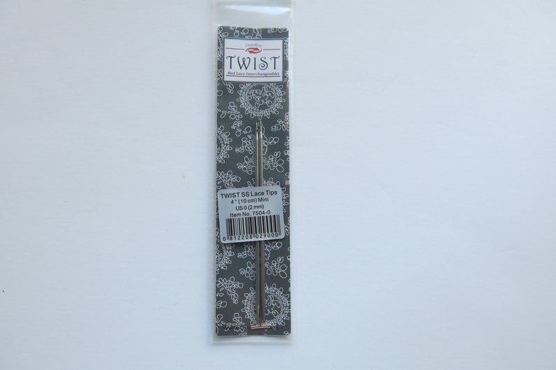 Peut inclure: Une aiguille Twist 95 Lace Tips argent&eacute;e dans un emballage en plastique sur fond gris. L'emballage porte l'inscription "Twist 95 Lace Tips 4" (10 cm) Mini US 0 (2 mm) Item No. 7594-0".