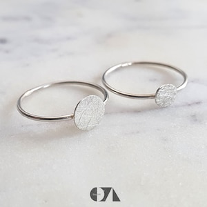 Könnte beinhalten: Zwei silberne Ringe mit einem strukturierten runden Design. Die Ringe sind schlicht und minimalistisch.