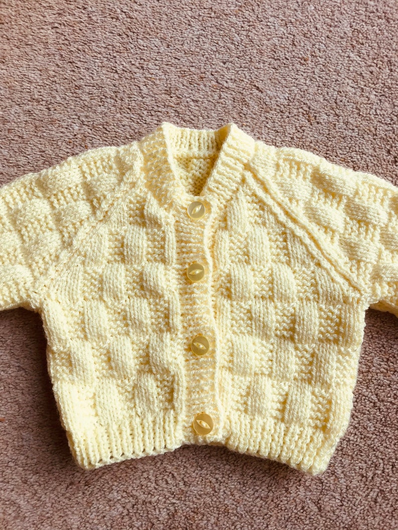 Pu&ograve; includere: Un cardigan per neonati lavorato a mano, di colore giallo chiaro, con un motivo a trama a cestino. Il maglione ha uno scollo a V, maniche lunghe ed &egrave; chiuso con quattro bottoni rotondi giallo chiaro. L'indumento &egrave; realizzato in filato morbido.