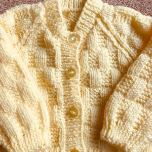 Pu&ograve; includere: Un cardigan giallo chiaro lavorato a mano, con scollo a V e maniche lunghe. Il maglione presenta un motivo a punto strutturato ed &egrave; chiuso con quattro bottoni rotondi e traslucidi. Il colore pastello tenue e il design accogliente suggeriscono un capo per neonati o bambini piccoli.