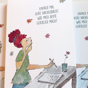 Könnte beinhalten: Drei Karten mit einer Aquarell-Illustration einer Person, die an einem Schreibtisch sitzt und in ein Notizbuch schreibt. Der Text auf den Karten lautet "Einfach mal kurz nachgedacht, was mich heute glücklich macht."
