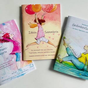 Könnte beinhalten: Drei farbenfrohe Notizbücher mit illustrierten Umschlägen. Jedes Notizbuch zeigt ein anderes Design mit einer Frau in einem farbenfrohen Outfit. Das erste Notizbuch ist rosa mit einer Frau, die eine gelbe Blume hält. Das zweite Notizbuch ist rosa und orange mit einer Frau, die Ballons hält. Das dritte Notizbuch ist blau und grün mit einer Frau in einer Yoga-Pose. Die Notizbücher sind mit "Inspirations-Sammlerin", "Ideen Sammlerin" und "Gedanken Sammlerin" betitelt.
