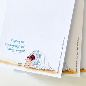 Könnte beinhalten: Stapel weißer Notizblöcke mit einer skurrilen Illustration eines Wesens in einer Muschel, mit dem Text "In jedem Tag schlummert ein kleines Wunder." Der Name des Künstlers und die Website sind ebenfalls sichtbar.