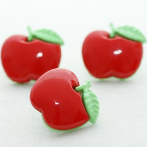 Könnte beinhalten: Drei rote knopfartige Äpfel mit grünen Blättern. Die Knöpfe sind glänzend und haben eine glänzende Oberfläche.
