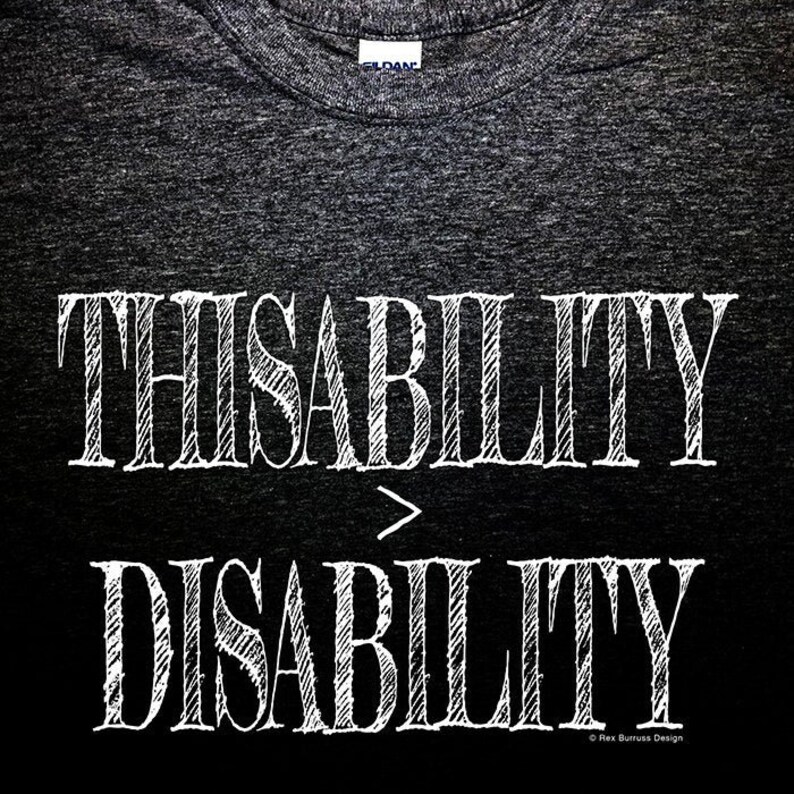 K&ouml;nnte beinhalten: Ein dunkelgraues T-Shirt mit dem Text "THISABILITY > DISABILITY" in wei&szlig;, schwarz umrandet und mit einem Schraffurmuster. Der Text ist mittig auf dem T-Shirt platziert. In der rechten unteren Ecke des T-Shirts steht der Text "Rex Burrus Design" in wei&szlig;.
