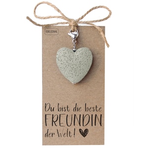 Peut inclure: Un porte-clés en forme de cœur gris avec un fermoir argenté et une carte brune qui dit "Du bist die beste Freundin der Welt!" (Tu es la meilleure amie du monde!).