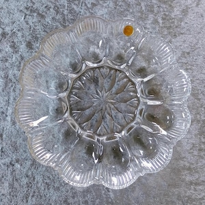 Puede incluir: Un plato de servir de vidrio transparente con un borde festoneado y un diseño central en forma de estrella. El plato tiene seis secciones para servir porciones individuales.