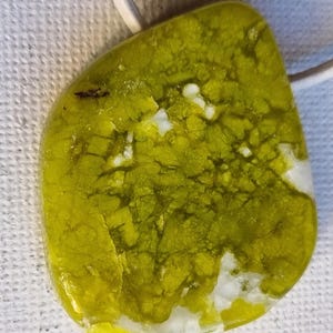 Peut inclure: Un pendentif en verre vert et blanc avec un effet marbré. Le pendentif est attaché à un cordon blanc.