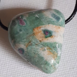 Peut inclure: Un pendentif en forme de cœur vert, blanc et rose avec un cordon noir. Le pendentif a un motif tourbillonnant et de petites inclusions rouges et roses.