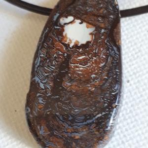 Könnte beinhalten: Ein brauner und weißer Opal-Anhänger mit einer silberfarbenen Kette. Der Opal hat ein wirbelndes Muster aus Braun, Weiß und Blau.