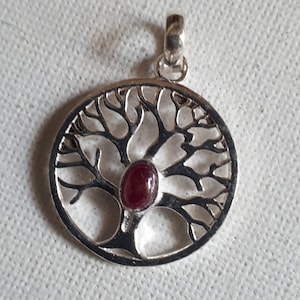 Può includere: Un ciondolo in argento a forma di albero della vita con una pietra preziosa rossa al centro.