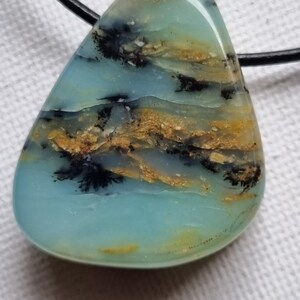 Può includere: Una collana con un ciondolo a forma di lacrima in opale blu chiaro, verde e oro. La pietra presenta inclusiones dendritiche nere.