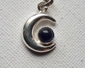 May include: A silver crescent moon pendant with a dark blue gemstone in the center.