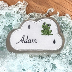 Peut inclure: Un patch en forme de nuage blanc avec une grenouille verte, deux gouttes de pluie et le nom "Adam" brodé en fil noir.