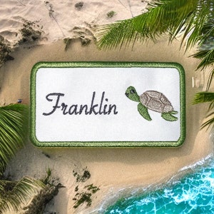 Peut inclure: Un patch brodé blanc avec une bordure verte. Le patch présente le nom "Franklin" en écriture cursive et une tortue de mer verte avec une carapace brune.