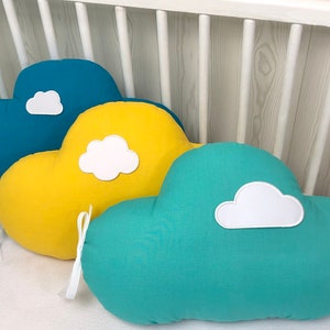 Peut inclure: Trois oreillers en forme de nuage dans un berceau. Les oreillers sont turquoise, jaune et turquoise clair. Chaque oreiller a un nuage blanc cousu sur le devant.