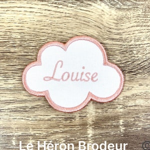 Peut inclure: Un patch brodé en forme de nuage rose avec le nom "Louise" brodé en fil blanc.