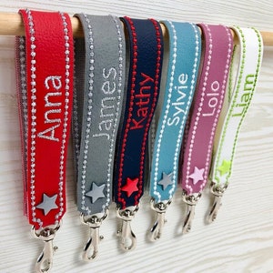 Könnte beinhalten: Sieben bunte Leder-Schlüsselanhänger mit silbernen Schlüsselringen und Stern-Anhängern. Jeder Schlüsselanhänger ist mit einem Namen personalisiert: Anna, James, Kathy, Sylvie, Lolo, Liam.