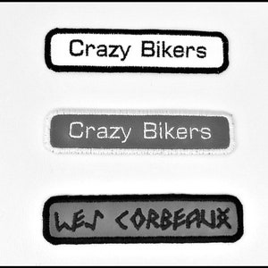 Peut inclure: Trois patchs rectangulaires avec des coutures noires autour des bords. Le patch du haut est blanc avec le texte "Crazy Bikers" en noir. Le patch du milieu est gris avec le texte "Crazy Bikers" en blanc. Le patch du bas est gris avec le texte "LES CORBEAUX" en blanc.