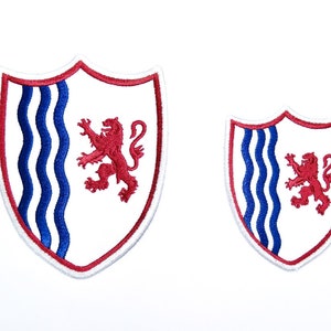 Può includere: Due toppe ricamate a forma di scudo. La toppa più grande è bianca con un leone rosso e linee ondulate blu. La toppa più piccola è dello stesso design ma più piccola.