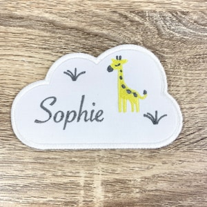 Peut inclure: Patch brodé en forme de nuage blanc avec une girafe jaune et le nom "Sophie" en lettres grises.
