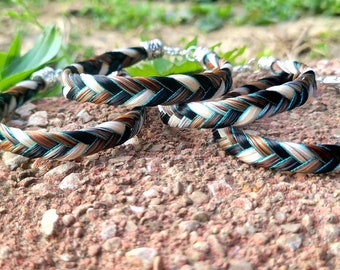 May include: A set of three braided bracelets made from strands of black, brown, and white hair, accented with thin metallic turquoise threads. Each bracelet features a silver-toned metal clasp and connector at the ends to secure the circular band.