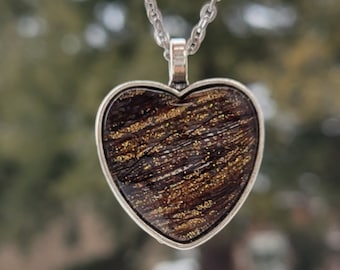 May include: A silver chain necklace with a heart-shaped pendant. The pendant is made of brown resin with gold glitter embedded in it.