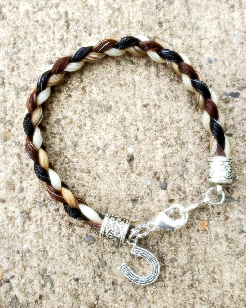 Peut inclure: Un bracelet tress&eacute; en crin de cheval avec des brins noirs, bruns et blancs. Le bracelet est orn&eacute; d'un charme en forme de fer &agrave; cheval argent&eacute; et de deux accents de perles argent&eacute;es.