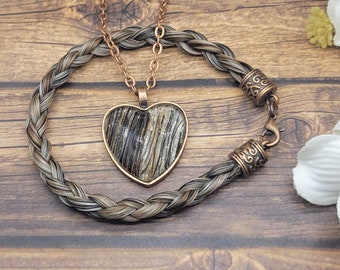 May include: A braided horsehair bracelet with copper accents and a matching necklace with a heart-shaped pendant. The pendant is made of clear resin with a brown and black pattern.