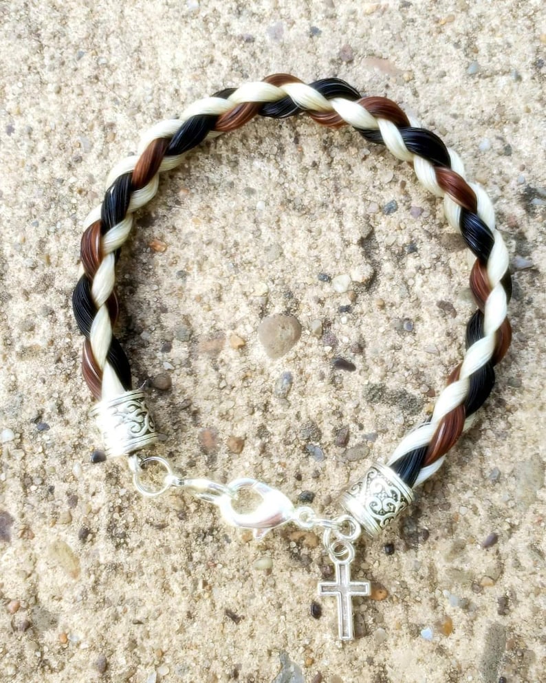 Peut inclure: Un bracelet tress&eacute; en crin de cheval noir, brun et blanc avec des accents argent&eacute;s. Le bracelet a un fermoir argent&eacute; et un charme argent&eacute; en forme de croix.
