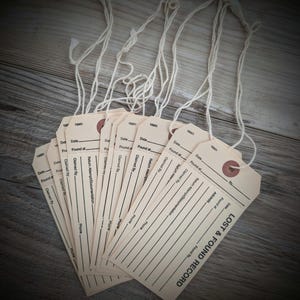 May include: A stack of beige paper tags with attached strings. Each tag has a reinforced hole and printed lines for information. The text "LOST & FOUND RECORD" is printed on the bottom right corner of each tag.