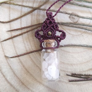 Peut inclure: Un collier en macramé violet avec une petite bouteille en verre remplie de cristaux blancs. La bouteille a un bouchon en liège et est attachée à un cordon brun.