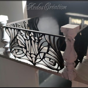 Puede incluir: Una barandilla de balcón de metal negro con un diseño decorativo. La barandilla está unida a columnas pintadas de blanco.