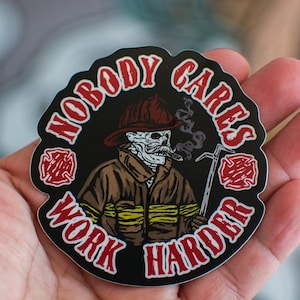 May include: A black and red round sticker with a skeleton firefighter wearing a red helmet and holding a hook. The sticker says "Nobody Cares Work Harder" in a red circle around the firefighter.