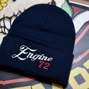 May include: A navy blue beanie with a white embroidered cursive word "Engine" and the number "72" in red.