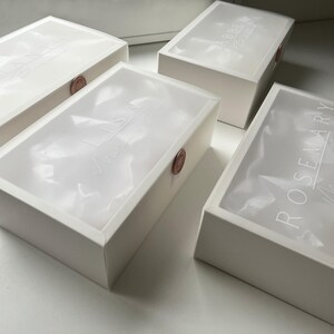 May include: Four white rectangular boxes with translucent lids. The lids have white text and are sealed with a round, reddish-brown wax seal. The boxes are arranged on a white surface.