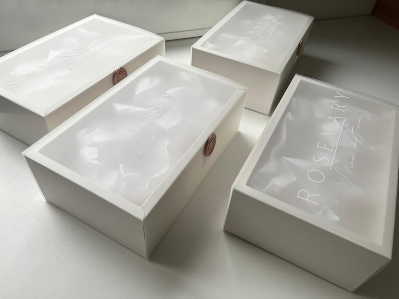 May include: Four white rectangular boxes with translucent lids. The lids have white text and are sealed with a round, reddish-brown wax seal. The boxes are arranged on a white surface.