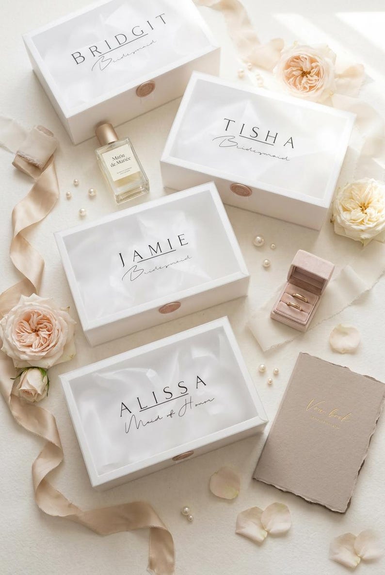 May include: White gift boxes with names like BRIDGIT, TISHA, JAMIE, and ALISSA printed on them. The boxes are sealed with a rose gold wax stamp. Other items include a perfume bottle, a ring box, and a vow book.
