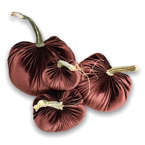 May include: Three burgundy velvet pumpkins of different sizes. The pumpkins are decorated with gold stems and have a soft, plush texture.