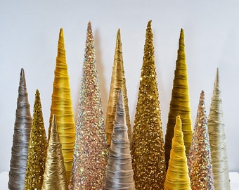 May include: A collection of 11 decorative cone-shaped Christmas trees in gold and silver. The trees are made of fabric and sequins.