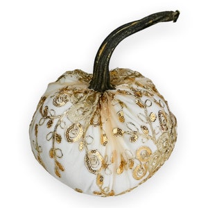 Puede incluir: Una calabaza blanca con encaje y lentejuelas doradas. La calabaza es un artículo decorativo para otoño y Halloween.