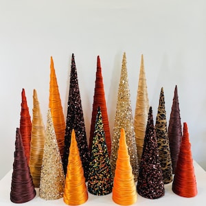 May include: A collection of 14 cone-shaped decorative trees in various shades of orange, brown, and gold. The trees are made of fabric and sequins, and some have a leopard print pattern.