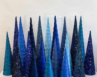 May include: A collection of blue and teal fabric Christmas trees of varying sizes and designs. The trees are decorated with sequins and are arranged in a staggered pattern.