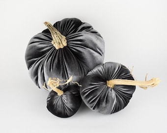 May include: Three gray velvet pumpkins with brown stems. The pumpkins are arranged in a cluster, with the largest pumpkin in the back and the smallest pumpkin in the front.