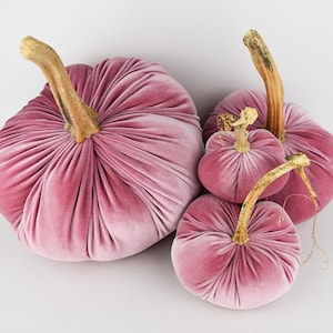 May include: Four velvet pumpkins in shades of pink. The pumpkins are arranged in a pyramid shape, with the largest pumpkin at the bottom and the smallest pumpkin at the top.