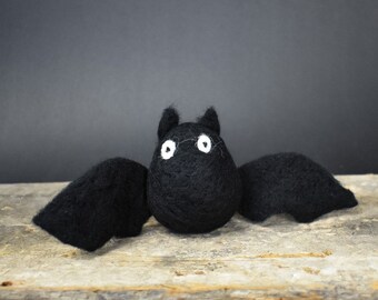 May include: A black felt bat with white eyes. The bat is sitting on a wooden surface.
